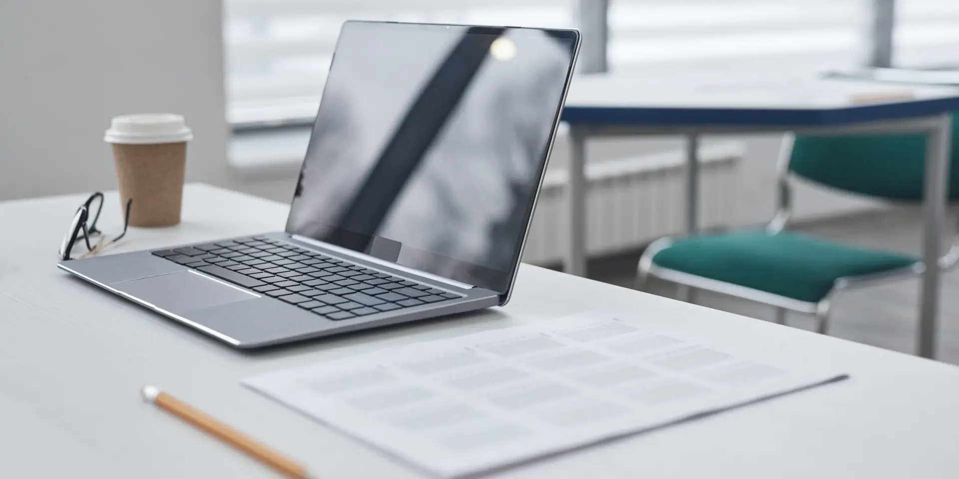 Bureau lumineux avec un ordinateur portable, un café à emporter, des lunettes et des documents